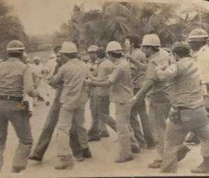 Trabajadores protegen a Miguel Medina, secretario general del gremio, ante la represión policial; Capellán, Báez, D Co, Germán y Lencho Paulino (EPD), fue brutalmente golpeado por un sargento mayor.